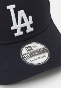 Cap azul-marinho com um logótipo bordado branco "LA", feito de tecido suave, com uma aba curva e acabamentos cosidos. Etiqueta de tamanho exibida.