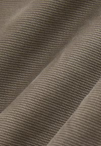 Tessuto testurizzato di un colore beige tenue, con un motivo intrecciato e una superficie liscia, che mostra una caduta morbida e flessibile.