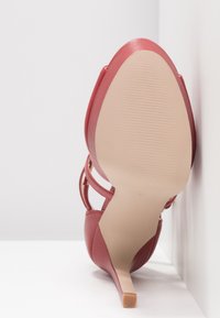 Chaussure à talon aigu rouge avec un bout pointu, un talon fin, en cuir lisse, et une semelle texturée, avec un design de strap.