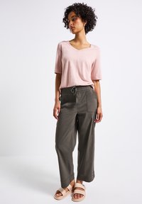 Haut rose clair à manches courtes avec un col en V, associé à un pantalon ample vert olive avec une taille élastique et des poches avant. Sandales plates.