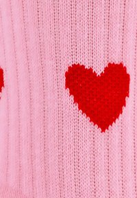 Pull en tricot rose avec des côtes verticales, orné de deux motifs de cœur rouges, mettant en valeur une texture douce et un contraste de couleurs éclatant.