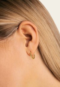 Pendiente de aro dorado con un diseño texturizado y retorcido. Visible en una oreja, destacando su forma circular y acabado brillante.