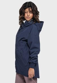 Marineblaue, wasserdichte Jacke mit Kapuze, elastischen Bündchen und verstellbarem Bund. Verfügt über eine frontale Reißverschlusstasche und ein schlankes, minimalistisches Design.