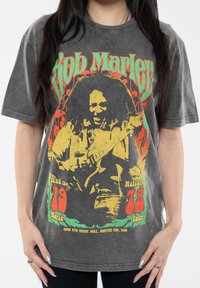 Gray oversized t-shirt featuring a colorful graphic of a musician with text detailing a tour date and location. Soft, worn fabric texture.