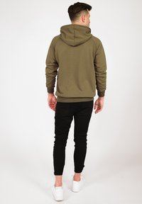 Olivgrön hoodie med dragsko i huvan, ribbade ärmslut och midja. Matchad med svarta slim fit-jeans och vita sneakers. Synliga söm detaljer.