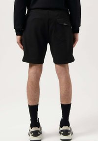 Black cotton men's shorts with an elastic waistband, side and back pockets, and a rectangular patch detail on the back pocket.