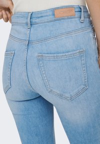 Svetloplave traperice visokog struka od trapera, s dvije stražnje džepove i smeđom kožnom zakrpom s brendom na pojasu.