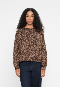 Pulóver so zvieracím vzorom leopard v hnedej a čiernej farbe, s dlhými rukávmi, okrúhlym výstrihom a voľným strihom, v kombinácii s tmavými džínsami.