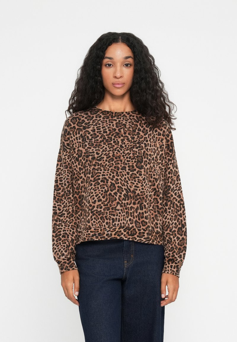Pulóver so zvieracím vzorom leopard v hnedej a čiernej farbe, s dlhými rukávmi, okrúhlym výstrihom a voľným strihom, v kombinácii s tmavými džínsami.