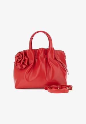 Sac à main en cuir rouge avec un détail froncé, une grande décoration en forme de rose sur le côté, deux poignées et une bandoulière amovible enroulée à côté.