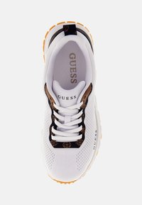 Sneaker bianco in rete con dettagli in pizzo neri, motivo logo marrone, suola imbottita e suola esterna arancione per la trazione. Nome del marchio 'GUESS' visibile.