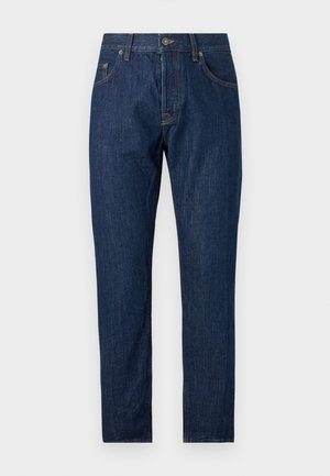 Męski model stoi z jedną ręką w kieszeni, nosi granatową bluzę z napisem "DONDUP", ciemnoniebieskie jeansy i brązowe sneakersy na białym tle.