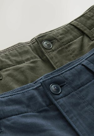 Izstādītas divas bikses. Vienas ir olīvzaļas, otras - tumši zilas, abām ir pogu aizdare un struktūrveida kokvilnas audums.