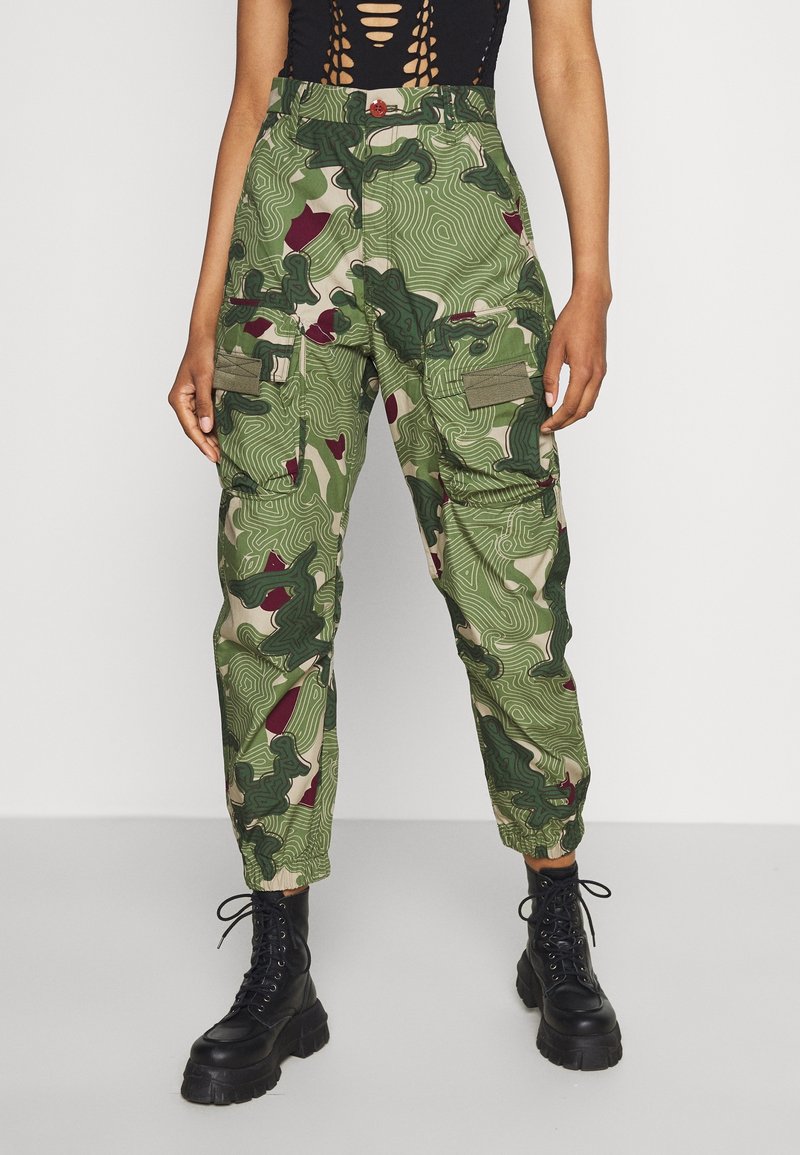 Cargo pants in a green and beige camouflage pattern. Features include multiple pockets, a drawstring hem, and a relaxed fit.