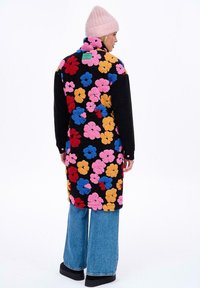 Dlhý čierny kabát s veľkými, farebnými kvetinovými aplikáciami v ružovej, modrej, červenej a žltej farbe. Spárované s rozšírenými džínsami a ružovou čiapkou.