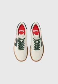 White fabric sneakers with green accents, dark laces, and a gum rubber sole. Red inner lining with 'CAMPER' branding on the tongue.