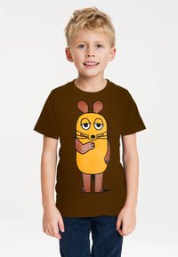Brown t-shirt featuring a cartoon character with an orange body, brown ears, and black whiskers, worn by a child with short blond hair.