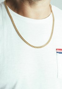 Necklace cu lanț de culoare aurie pe un tricou alb. Lanțul are inele interconectate cu o finisare netedă și lustruită.