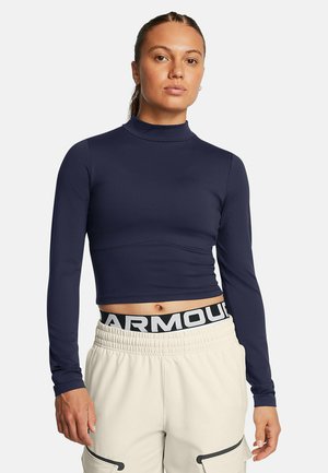 Marineblaues Langarm-Crop-Top mit hohem Kragen und taillierter Passform, hergestellt aus glattem Stoff. Kombiniert mit hellen Hosen mit elastischem Bund und Markenlogo.