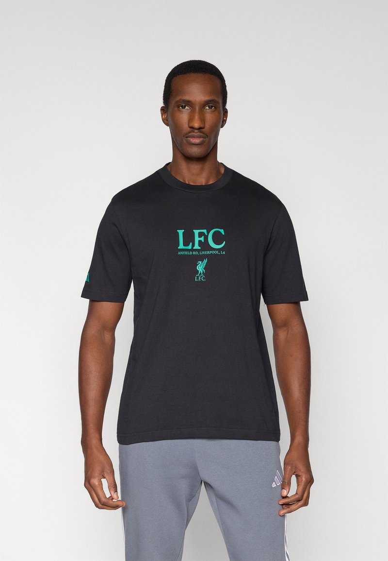 Czarny bawełniany t-shirt z zielonym logo "LFC", krótkimi rękawami i okrągłym dekoltem. Noszony z szarymi spodniami dresowymi.