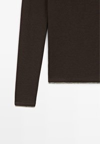 Brown long-sleeve top made of soft fabric with a fitted silhouette. Features a rounded neckline and a contrasting light-colored hem.