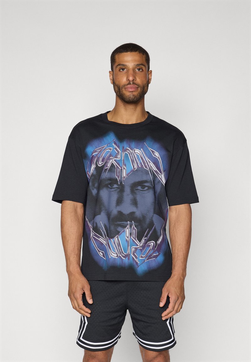 Camiseta de algodón negra con un gran estampado gráfico de una cara con acentos en azul y morado, cuello redondo y corte relajado.