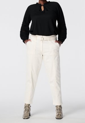 Top negro de manga larga con detalle de ojal, combinado con pantalones crema de tiro alto con presillas para cinturón y bolsillos; botines de serpiente.