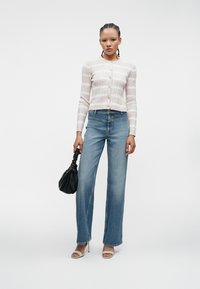 Ανοιχτό ροζ ριμπ κασκόλ με κουμπιά, μπλε τζιν ψηλής μέσης, διαφανή τακούνια και μια υφασμάτινη μαύρη τσάντα. Απλή λευκή φόντο.