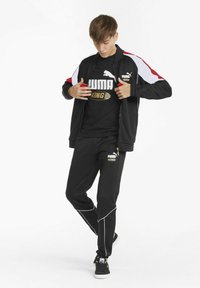 Sort atletisk træningstøj med røde og hvide accenter, bestående af en jakke med lynlås, sort t-shirt med guld logo og matchende bukser med hvide syninger.