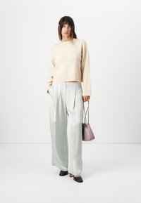 Beige wool sweater with a cropped design, paired with light grey, wide-leg satin trousers. Holding a small lavender handbag, wearing black heels.