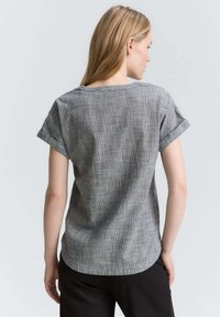 Haut à manches courtes à carreaux gris avec une coupe décontractée, présentant un col rond et des poignets retournés. Tissu doux avec une finition texturée.