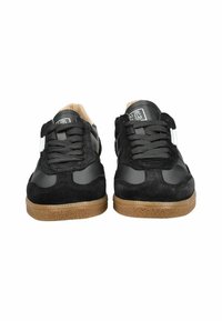 Un paio di sneakers nere con lacci, suole in gomma marrone e dettagli bianchi, esposte frontalmente su uno sfondo bianco.