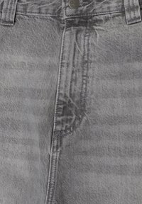 Gros plan d’un jean en denim gris montrant une braguette zippée, une fermeture à bouton, des passants de ceinture et des détails de couture texturés.