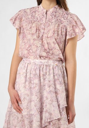 Femme portant un chemisier marbré rose pastel et violet avec un yoke plissé et des manches volantées, assorti à une jupe à volants assortie.