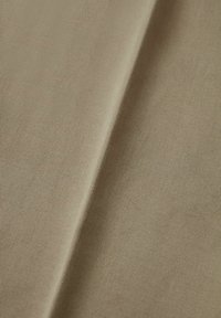 Beige ribbat tyg med en slät textur och subtil lyster, som visar ett konsekvent mönster av fina linjer och mjuka veck.