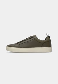 Oliven grøn sneakers med en glat tekstur, med gummisål, mørke snørebånd og en sort løfteløkke bagpå.
