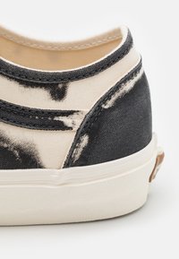 Canvas sneaker featuring a black and cream color scheme with a textured finish, contrasting stitching, and a rounded toe, set on a white sole.