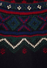 Tissu tricoté avec des motifs géométriques en rouge, vert, bleu, blanc sur fond noir, avec des zigzags, des losanges et de petites formes regroupées.