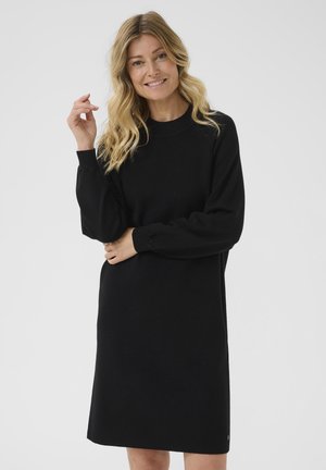 Rochie neagră cu mânecă lungă, cu guler rotund, croială lejeră, manșete ribbed și material moale și texturat. Lungime până la genunchi, cu detalii subtile.