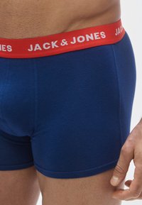 Boxers de algodão azul marinho com uma cintura vermelha com a inscrição "JACK & JONES" em letras brancas. Textura suave e design ajustado.