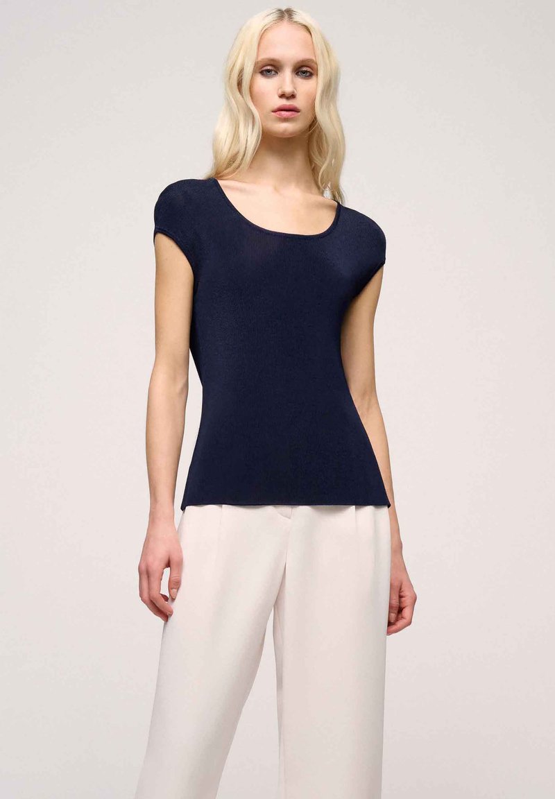 Top tricotat de culoare bleu navy, cu decupaj rotund la gât și mâneci scurte, având o siluetă ajustată și material texturat. Asortat cu pantaloni deschiși.