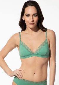 Grünes Bralette mit Spitzenbesatz und verstellbaren Trägern. Weicher Baumwollstoff, dreieckige Körbchen und zarte Spitzenverzierung entlang des Ausschnitts.