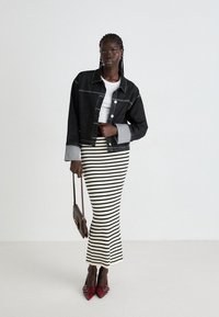 Black denim jacket with gray cuffs, white fitted top, and a long striped skirt in black and white, complemented by red pointed-toe heels and a brown handbag.