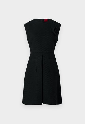 Čierne šaty s textúrovaným vzorom, s krátkymi rukávmi, dvoma prednými vreckami a kvetinovým akcentom na ramene. Zapínanie na zips na chrbte.
