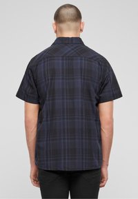 Camicia a maniche corte in plaid nei toni navy, nero e blu. Presenta un colletto classico e una vestibilità rilassata con orlo dritto.