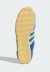 Plava potplat tenisica s teksturiranom bež gumom. Ima cik-cak uzorak, "adidas" logo i tri bijele pruge duž strana.