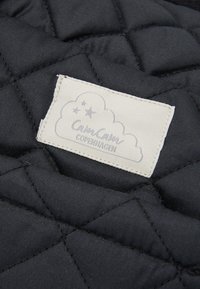 Sort quiltet stof med en hvid rektangulær label syet på, der har et design med en sky og stjerner samt teksten "Cam Cam Copenhagen".