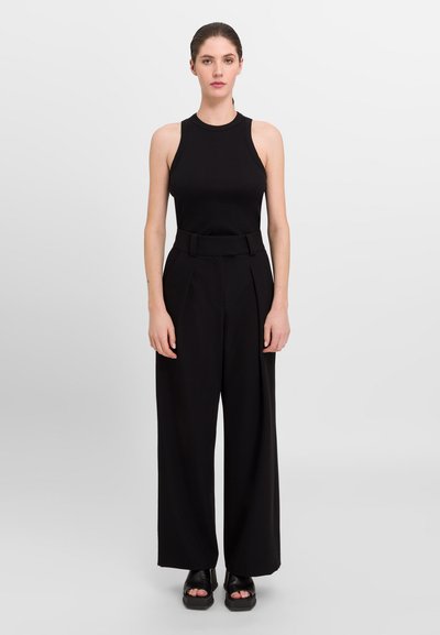 Must mustata top ilma varrukat, mis on kombineeritud kõrge vöökohaga ja laia säärega mustade pükstega. Riietusel on sile tekstuur ja minimalistlik disain.