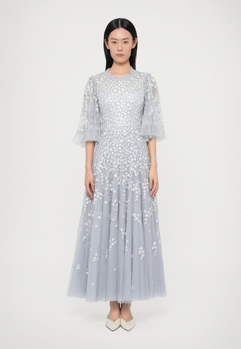 Długa, jasnoniebieska sukienka z prześwitującego materiału z kwiatowym haftem i falbanianymi rękawami, z dopasowanym gorsetem i zwiewną spódnicą.