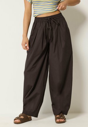 Person iført løse sorte bukser med snoretræk i taljen, stribet gul og blå cropped top og brune åbne sandaler med spænder.